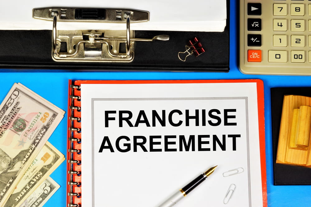 Franchise agreement document with calculator and cash illustrating FDD financial disclosures and initial investment costs.