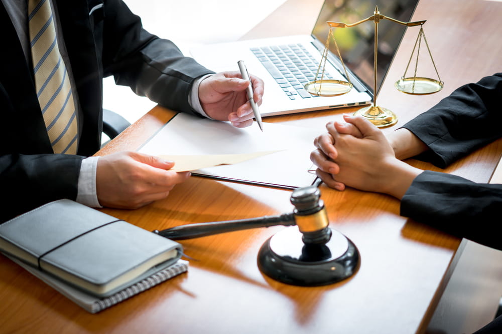 Attorney reviewing business contract terms with client at desk with scales of justice